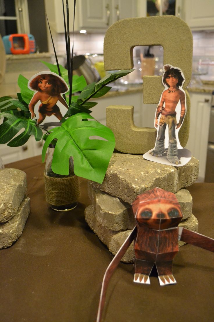 The Croods birthday invitation with cave family, tropical leaves, rocks, mammoth, and warm prehistoric colors