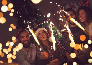 Group of young friends having fun at a New Year's celebration, holding sparklers at a midnight countdown.