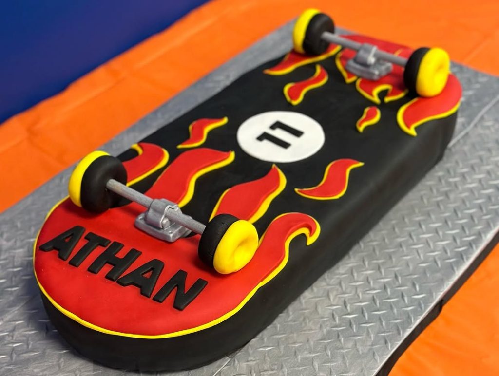 Skateboard birthday cake with fondant flames and black-yellow skateboard wheels