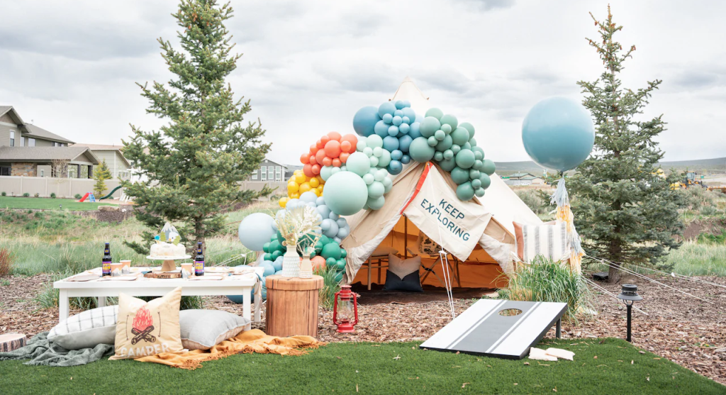 A cascade of colorful balloons in shades of blue, green, orange, and yellow creates a whimsical arch over the entrance. A giant, light blue balloon floats high above like a friendly sky-whale